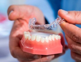 a person holding Invisalign aligners and a model of teeth