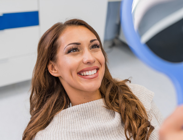 Woman smiling at reflection in handheld mirror
