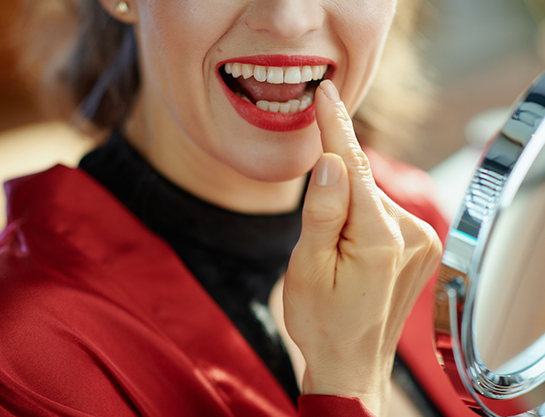 Woman using mirror to examine her teeth