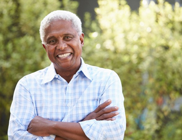 Senior man in light blue shirt smiling with arms folded