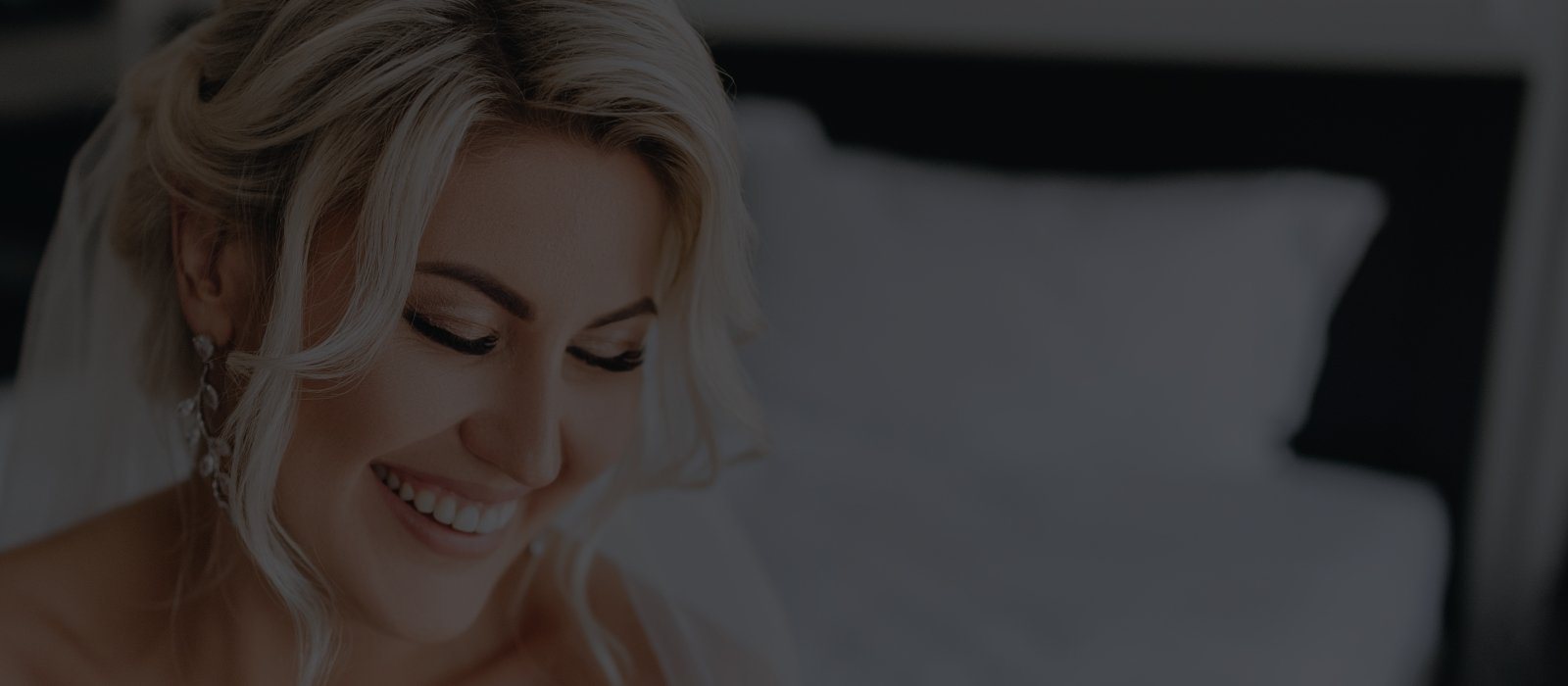 Smiling blonde woman sitting on bed with white sheets