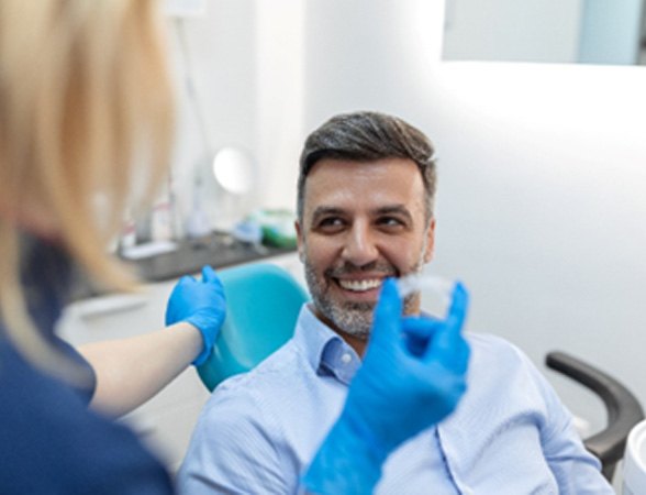 Man smiling at dentist holding Invisalign aligner