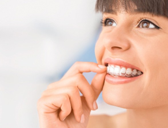 Woman smiling while putting Invisalign aligner on