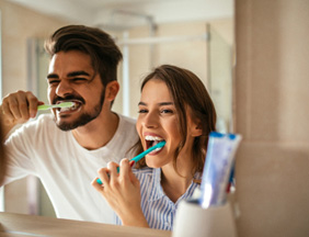 Couple smiling while brushing teeth in bathroom
