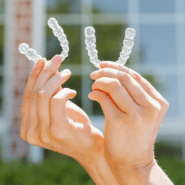 A person holds two clear braces outside Anthony Dillard, DDS Family & Cosmetic Dentistry building.
