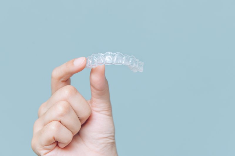Hand holding a clear aligner in front of a light blue background