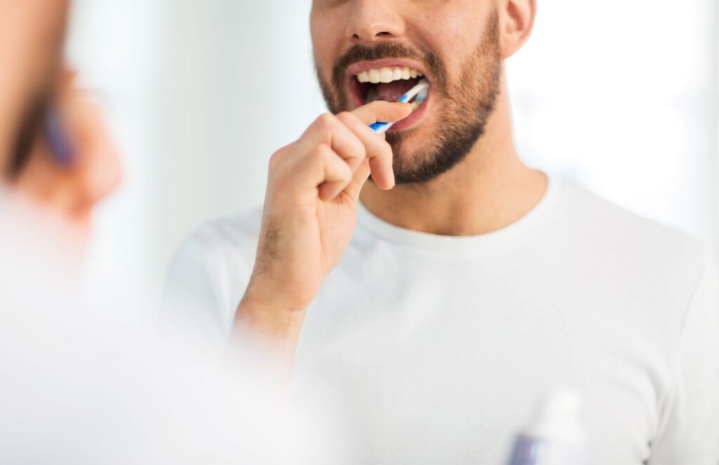 Nose-to-chest view of man in white shirt brushing teeth